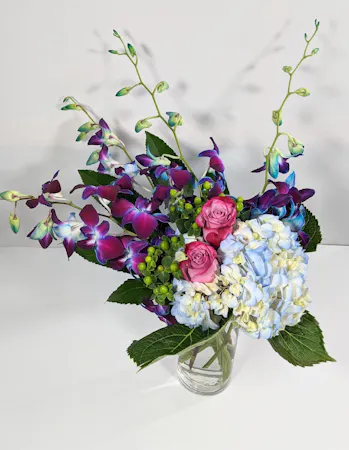 Blue dendrobium orchids paired with blue hydrangea & green hypericum hand-designed in a clear glass vase.