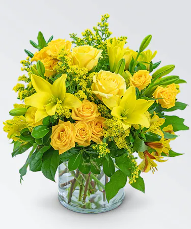 Yellow roses, alstroemeria, Asiatic lilies and more with foliage in a clear glass vase