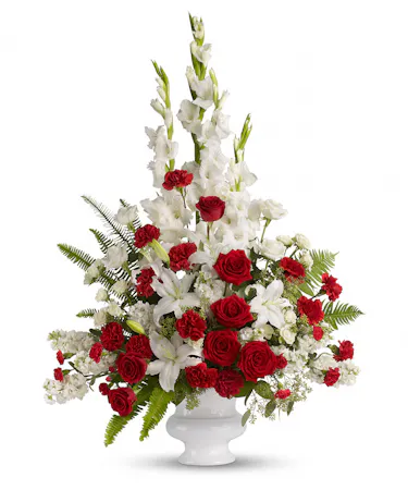 A white urn is filled with white and red flowers: lilies, roses, carnations and more