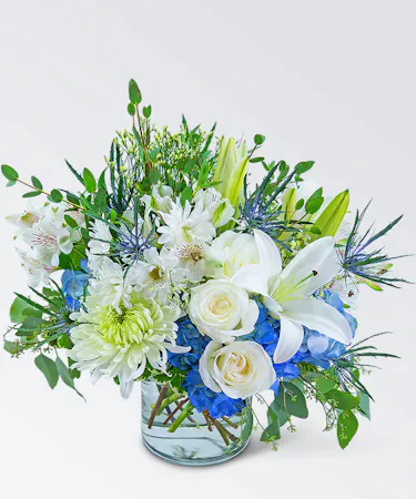 Bouquet of blue and white cut flowers with foliage in a clear glass vase