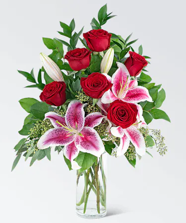 Red roses, stargazer lilies and greenery in a clear glass vase