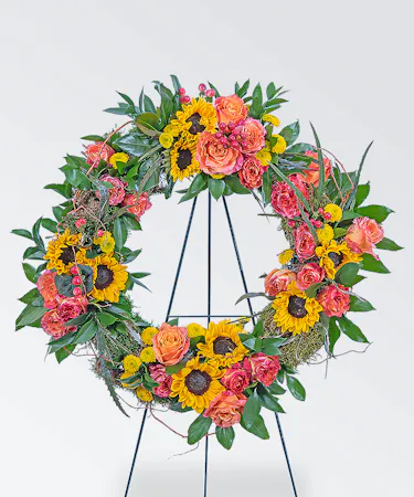 Funeral wreath with sunflowers, orange roses, greenery delivered on an easel for the service