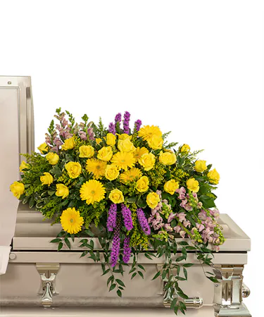 Casket spray of bright yellow and purple flowers with premium foliage
