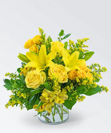 Cheerful bouquet of all-yellow flowers and foliage in a clear glass vase