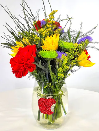 A rhinestone apple embellishes a stemless wine glass from Queen's Jewels and is filled with bright yellow, red and green flowers; daisies, carnations, button mums