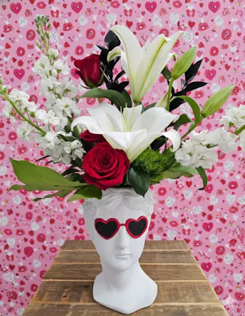 This edgy Valentine's gift features a cool sunglass-wearing bust filled with red roses, white lilies, and dark foliage.