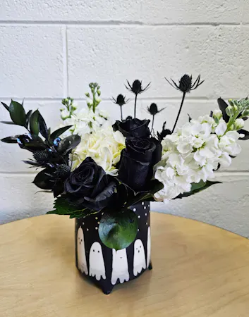 A black ceramic pot decorated with ghosts filled with white stock, hydrangea, black accents