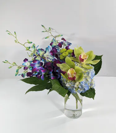 Blue dendrobium orchids paired with blue hydrangea & green hypericum hand-designed in a clear glass vase.