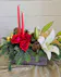 A wooden box with red candles, white lilies, red roses, winter greens, gold accents, elegant and fragrant centerpiece