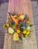 a single taper candle nestled in a Thanksgiving arrangement of orange carnations, fall chrysanthemums, green button mums and fall foliage and accents