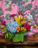 A leaf wrapped glass cube with blue hydrangea, purple carnations, eryngium, sunset leucadendron and greenery