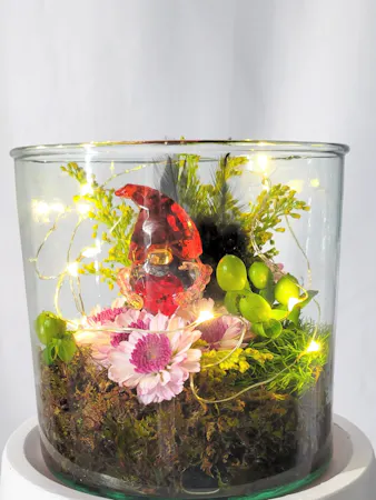 Our cute Heart Gnome is nestled on a bed of moss and accented with lavender button mums, green hypericum, yellow solidago and a tiny string of fairy lights