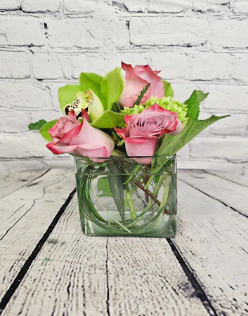 Green hydrangea and cymbidium orchids with lavender roses in a clear glass cube