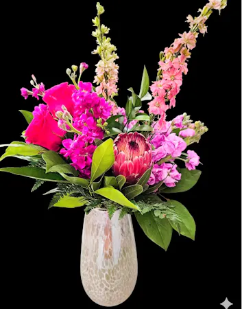 White iridescent vase with pink protea, pink roses, stock, larkspur and lush greenery