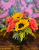 Sunflowers, orange roses, eryngium and solidago in a clear glass cube