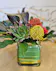 3 pincushion protea, 2 succulents, tropical foliage, a gold leaf-lined cube, and black ti leaf in a modern style design