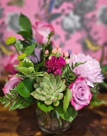 Lavender roses, lavender chrysanthemums, lime green button mums, red hypericum berry, a succulent in a short glass cylinder