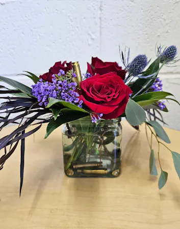 Compact vase of red roses, purple statice and shell casings