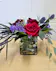 Compact vase of red roses, purple statice and shell casings