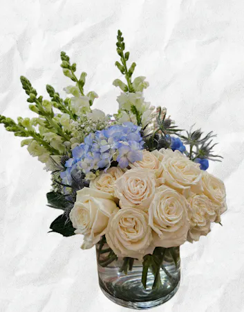 White roses, blue hydrangea, stock and eryngium in a clear glass vase