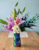 A stunning floral arrangement featuring pink Stargazer lilies, exotic blue orchids, and white hydrangeas in an iridescent vase.