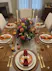 Purple stock, hot pink carnations, pincushion protea, chrysanthemums, roses, fall foliage Thanksgiving centerpiece