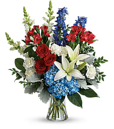 Patriotic bouquet of red, white and blue flowers and greenery in a clear glass vase