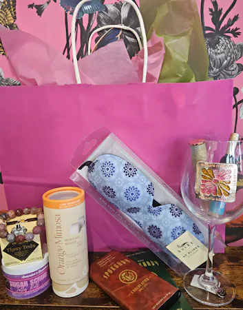 Our Wine Down gift bag includes a Queen's Jewels  wine glass,  chocolate bars, a bracelet, Mimosa cocktail cubes, Tipsy Treats gummy candy and more