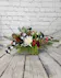 A rustic wooden container, add fragrant winter greens, burgundy carnations, white chrysanthemums, black & white ribbon and silver balls